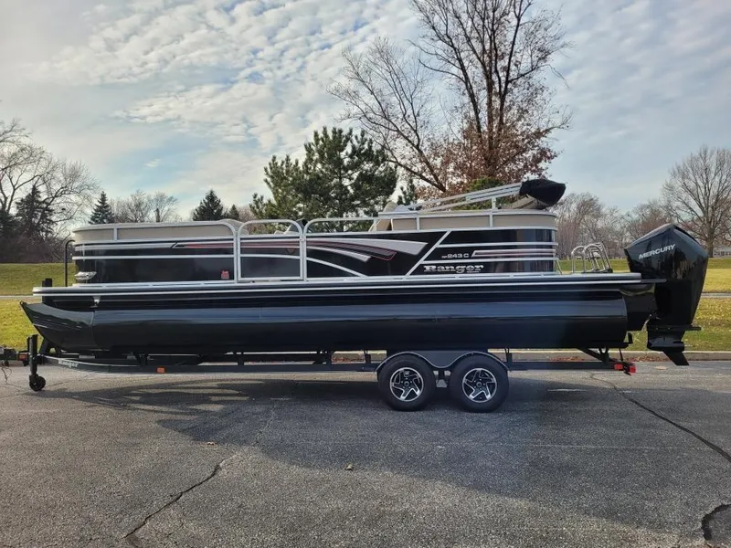 The Image of 2023 Ranger Reata 243C pontoon boat on a trailer in a park setting. - 0
