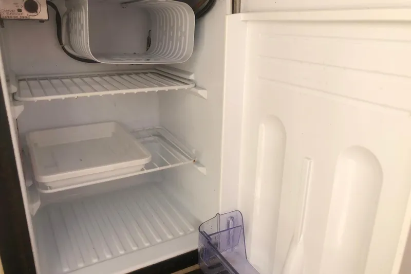 Slide: The Image of Empty refrigerator inside a 2001 Sea Ray 280 boat, showing shelves and storage compartments. - 24