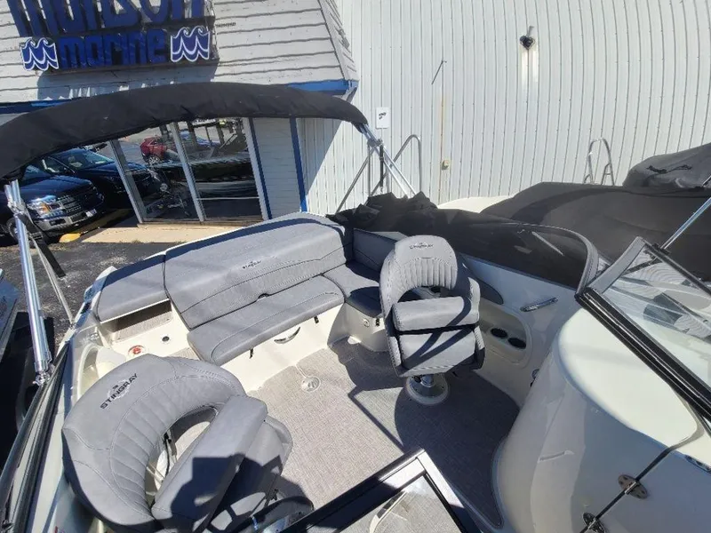 Slide: The Image of 2022 Stingray 215LR boat interior with gray seating and canopy at a marine dealership. - 7