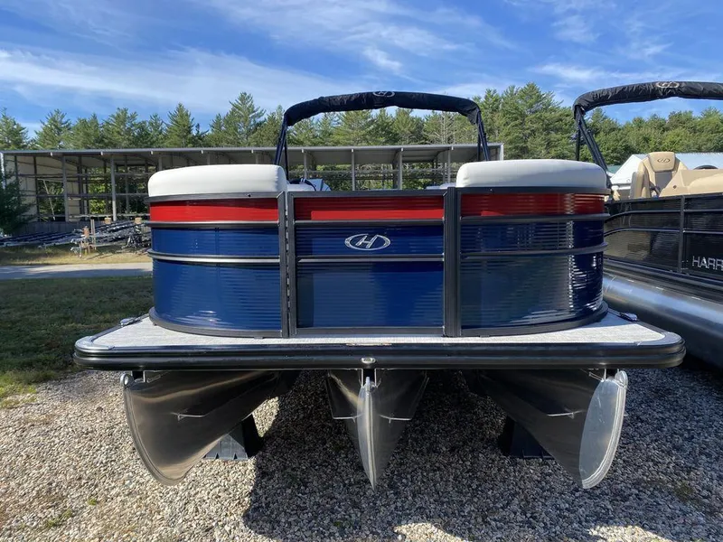Slide: The Image of 2023 Harris Cruiser 230 CWDH pontoon boat, blue and red, parked on gravel. - 3