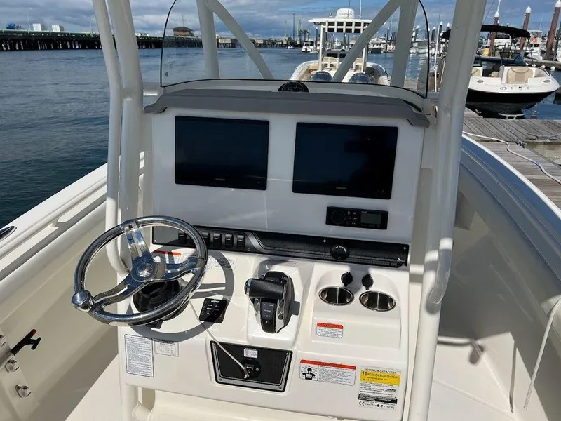 Slide: The Image of 2020 Mako 236 CC boat console with dual screens and steering wheel, docked by the water. - 5