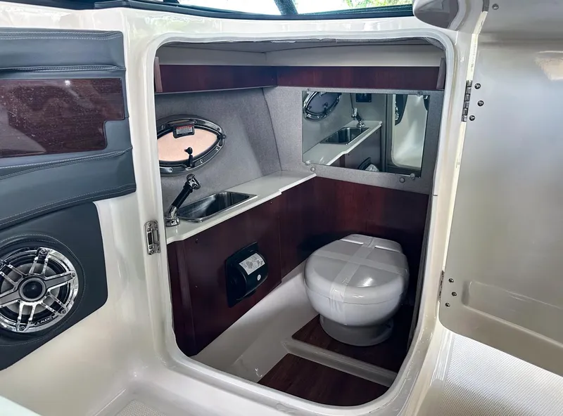 Slide: The Image of 2025 Chaparral 270 OSX OB boat interior with toilet, sink, and wood accents. - 20