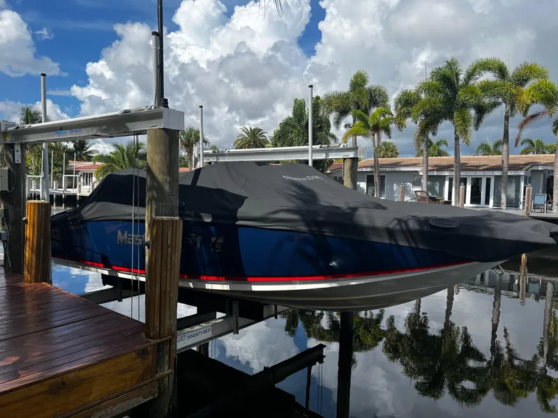 Slide: The Image of 2014 MasterCraft X-55 boat docked with cover, surrounded by palm trees and waterfront homes. - 2