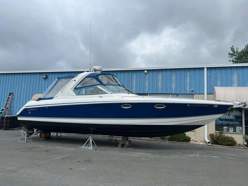 The Image of 2003 Formula 330 Sun Sport boat on stands, blue and white exterior, parked outdoors. - 0