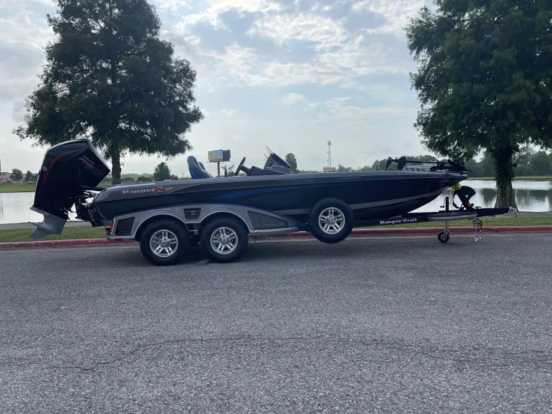 Slide: The Image of 2023 Ranger Z520R boat on trailer by a lake with trees in the background. - 0