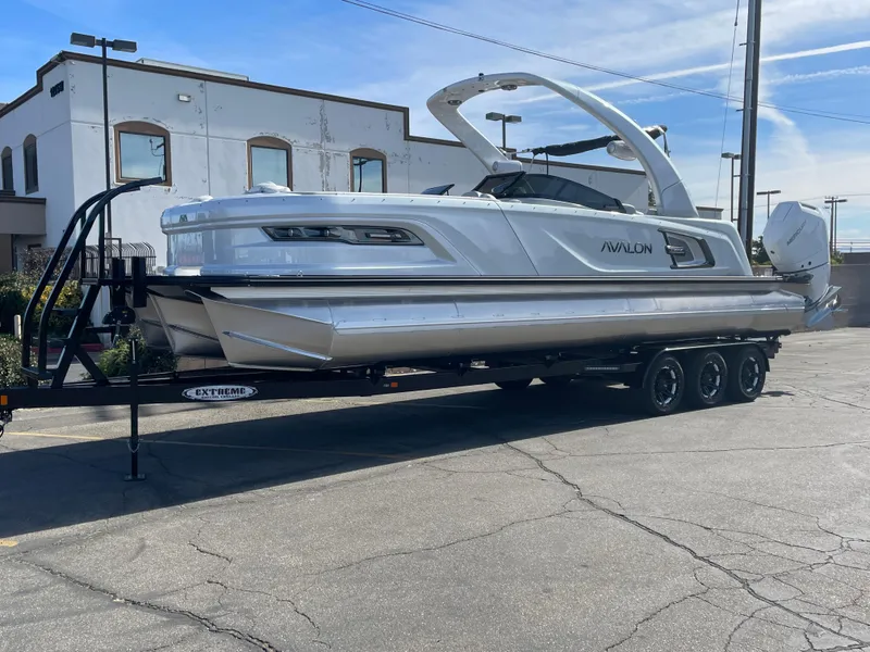 Slide: The Image of 2025 Avalon 2785 Excalibur Elite-Carbon Fiber boat on trailer, parked outdoors. - 2