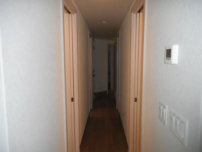 Slide: The Image of Narrow hallway with wooden floor and white walls, featuring multiple doors and a thermostat. - 28
