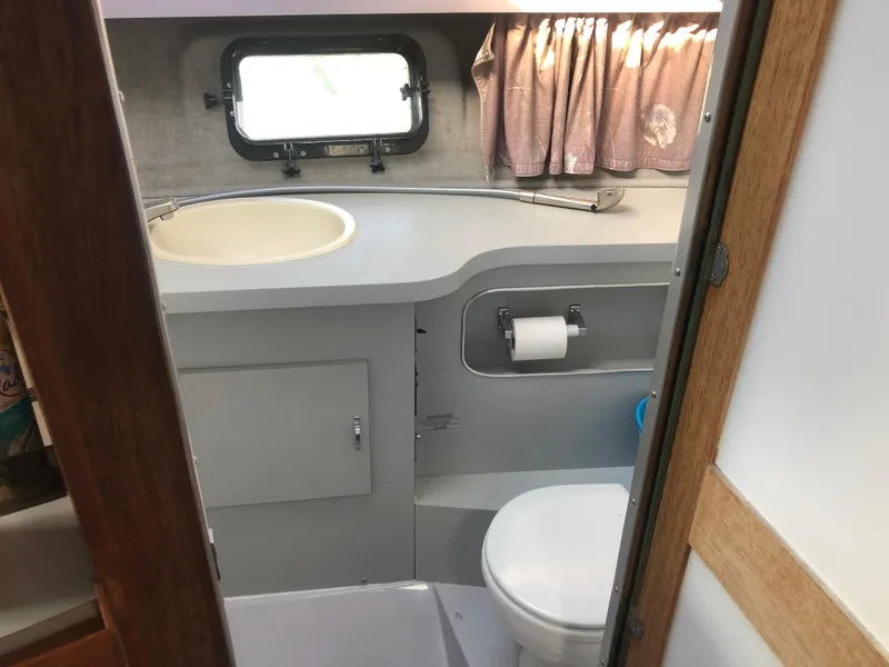 Slide: The Image of 1986 Cruisers ESPRIT 3370 boat bathroom with sink, toilet, window, and curtains. - 13