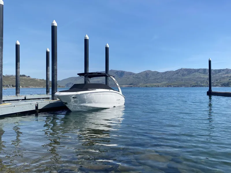 The Image of 2023 Regal LS6 Surf boat docked on a clear lake with mountains in the background. - 0