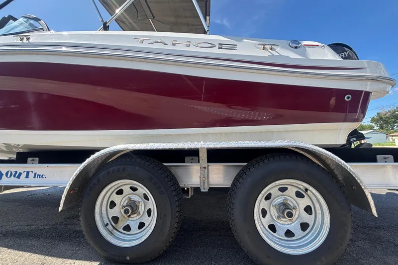 Slide: The Image of 2019 Tahoe 550 TF boat on trailer, featuring maroon and white design under clear blue sky. - 65