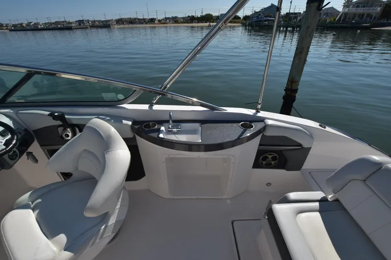 Slide: The Image of 2012 Regal 24 FasDeck boat interior with seating and sink, docked by calm waters. - 13