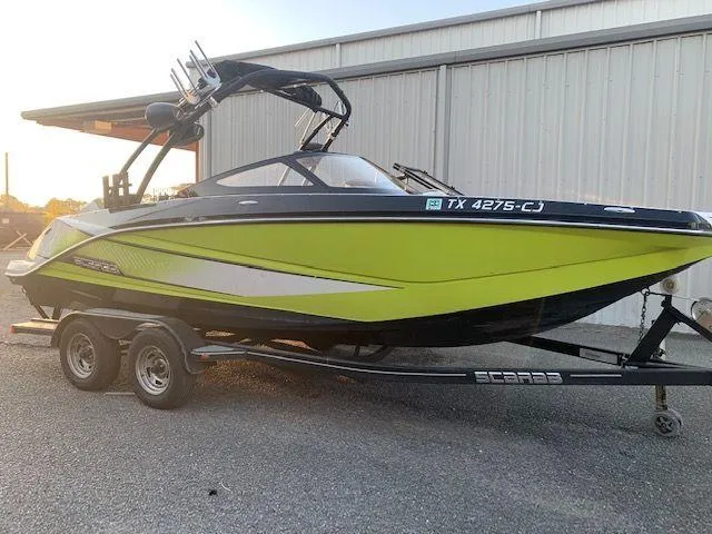 Slide: The Image of 2014 Scarab 215 boat on trailer, lime green and black, parked near a metal building. - 19