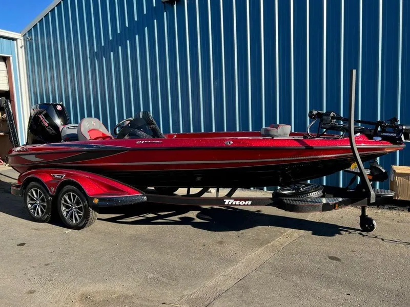 Slide: The Image of 2023 Triton 21 TrX Patriot bass boat on trailer, red and black, parked outside. - 6