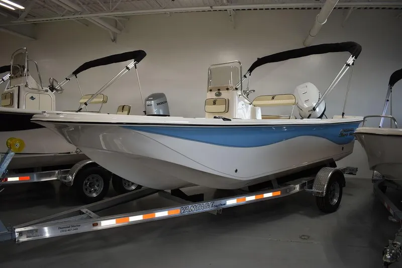 Slide: The Image of 2023 Carolina Skiff 19 LS boat on trailer in showroom, featuring blue and white design. - 2