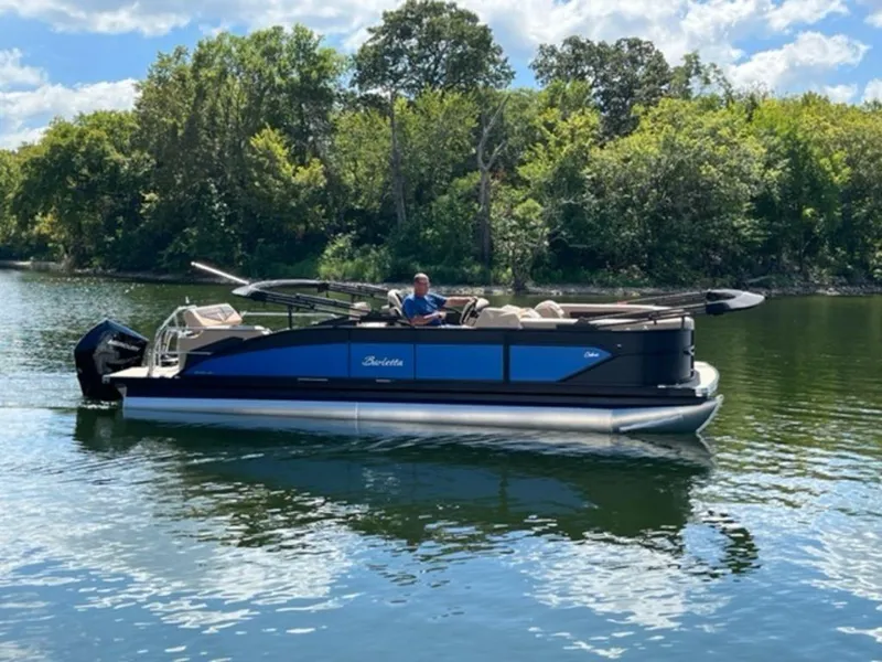 Slide: The Image of 2023 Barletta Cabrio 24 UE pontoon boat on a serene lake with lush green trees. - 2