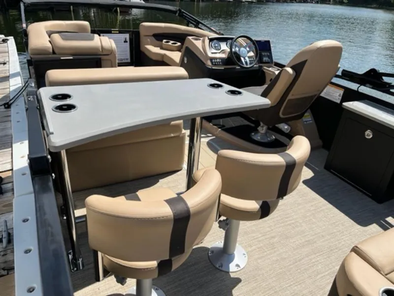 Slide: The Image of 2023 Barletta Cabrio 24 UE boat interior with beige seating and table, docked by the water. - 9