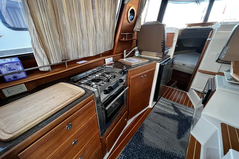 Slide: The Image of 2021 Ranger Tugs R-29S interior kitchen with stove, sink, and wooden cabinetry. - 13