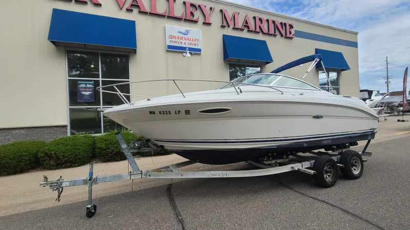 Slide: The Image of 2002 Sea Ray 225 Weekender boat on a trailer outside a marine dealership. - 2