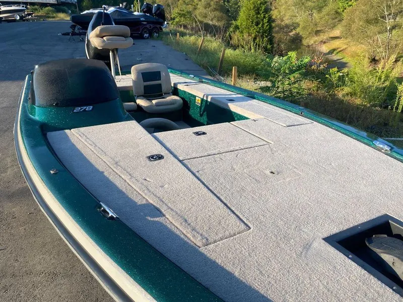 Slide: The Image of 2002 Bumble Bee 18 boat with spacious deck and seating, parked outdoors. - 9