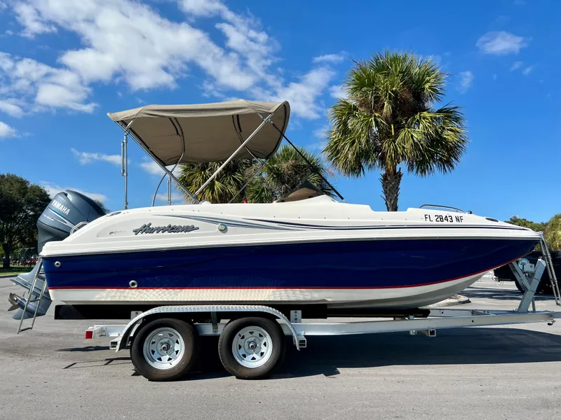 Slide: The Image of 2006 Hurricane 194 boat on trailer, blue and white, parked near palm trees. - 10
