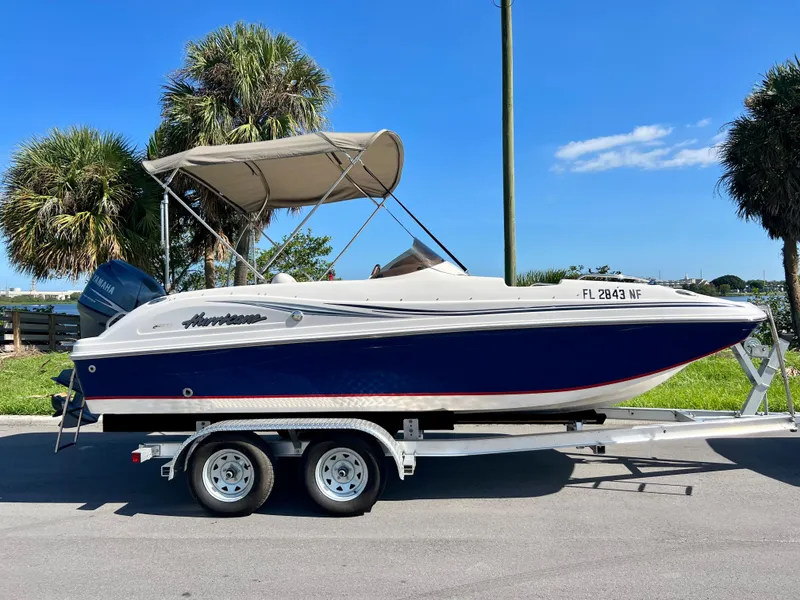 Slide: The Image of 2006 Hurricane 194 boat on trailer, blue and white, parked near palm trees. - 14