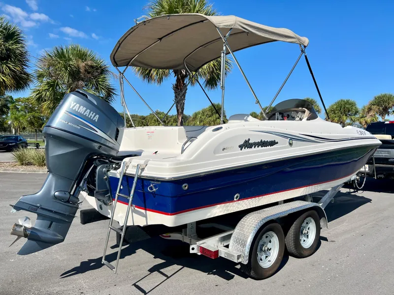 Slide: The Image of 2006 Hurricane 194 boat with Yamaha motor on trailer, parked under palm trees. - 2