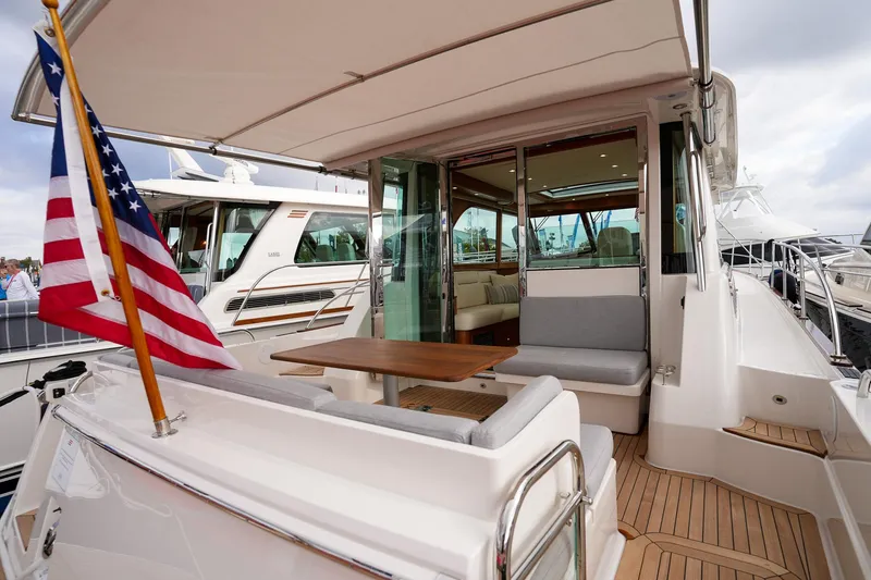 Slide: The Image of 2025 Sabre 45 Salon Express yacht with American flag, elegant deck seating, and wooden table. - 17