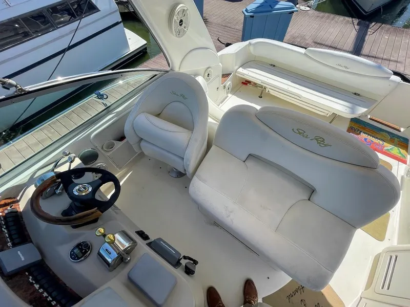 Slide: The Image of 2002 Sea Ray 340 Sundancer cockpit with helm, seating, and docked boat in background. - 23