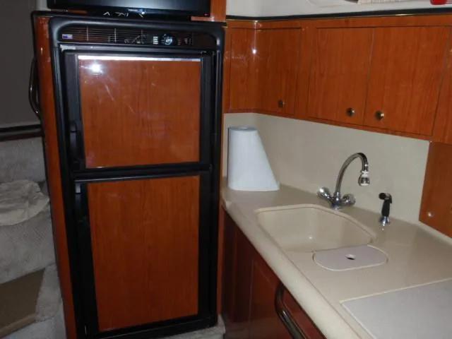 Slide: The Image of 1999 Sea Ray 410 Express Cruiser kitchen with wood cabinets and compact fridge. - 19