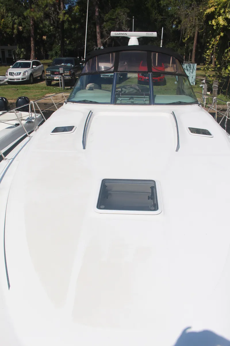 Slide: The Image of 1999 Sea Ray 410 Express Cruiser boat docked, front view, with trees and cars in background. - 45