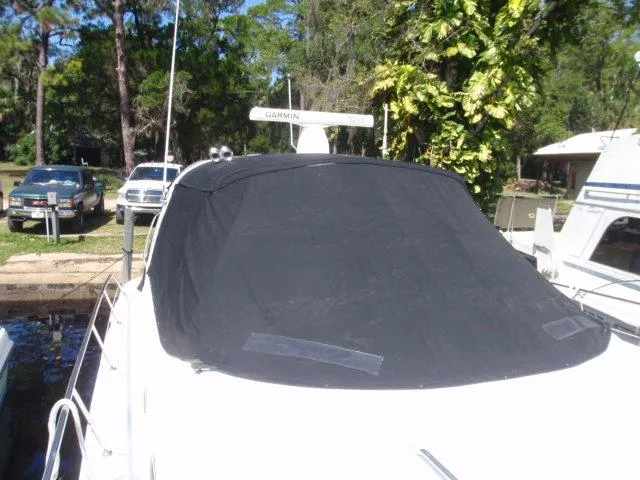 Slide: The Image of 1999 Sea Ray 410 Express Cruiser with black cover docked near trees. - 49