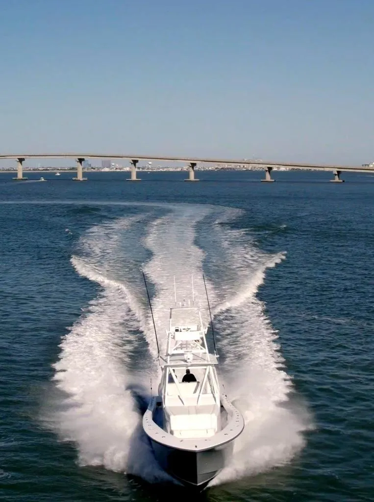 Slide: The Image of 2021 Conch 47 boat speeding on water near a bridge under clear blue sky. - 15