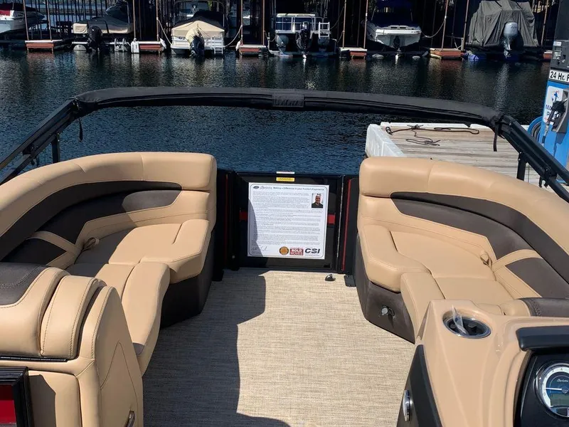 Slide: The Image of 2023 Barletta Cabrio 24UE pontoon boat interior with tan seating at a marina. - 2