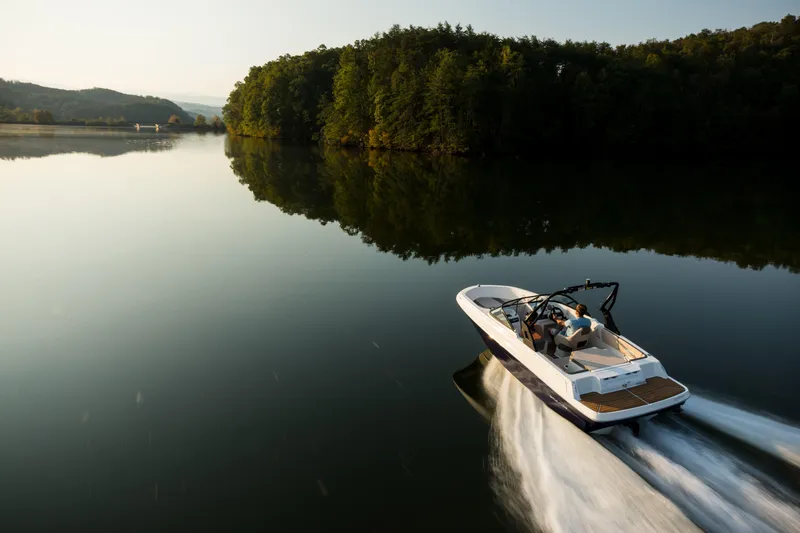 Slide: The Image of 2023 Bayliner VR4 OB boat cruising on a serene lake with lush green surroundings. - 24