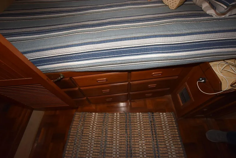 Slide: The Image of 1983 Krogen Trawler interior with striped bedding, wooden drawers, and woven rug. - 23