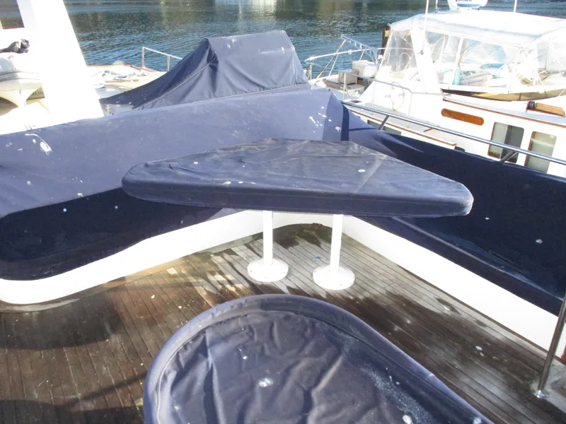 Slide: The Image of 1984 McQueen Flush Deck Motoryacht deck with covered seating and table, docked by the water. - 19