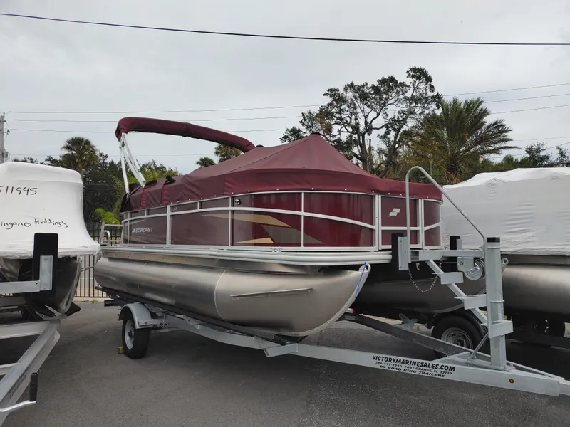 Slide: The Image of 2024 Starcraft EX 18 F pontoon boat on a trailer, covered with a maroon canopy. - 2