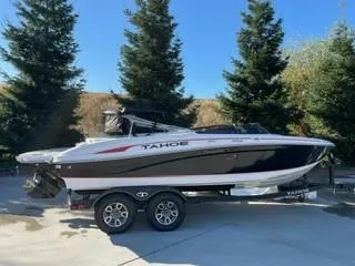 Slide: The Image of 2023 Tahoe 210 Si Limited boat on trailer, parked outdoors with trees in background. - 0
