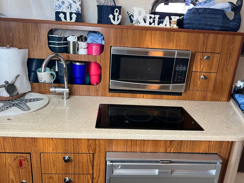 Slide: The Image of 2014 Pursuit 345 OS boat kitchen with microwave, sink, and stove. - 11