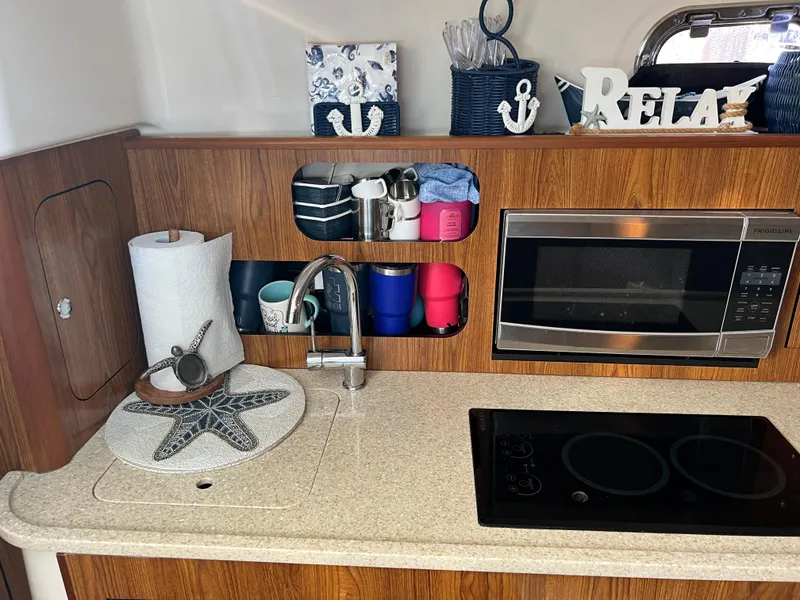Slide: The Image of 2014 Pursuit 345 OS boat kitchen with sink, microwave, and stove. - 13