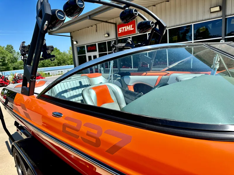 Slide: The Image of 2023 Sanger 237 SX boat in orange, parked outside a dealership. - 2