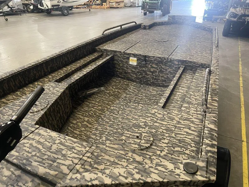 Slide: The Image of 2023 Legend Craft Outlaw 1656 camo-patterned boat interior in a warehouse. - 17