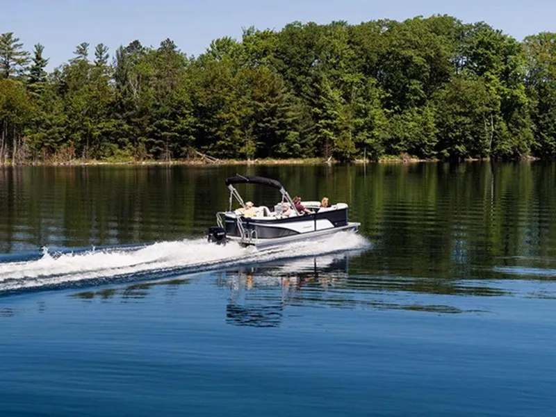 Slide: The Image of 2023 Crest Classic LX 240 SLRC CPT pontoon boat cruising on a serene lake. - 3