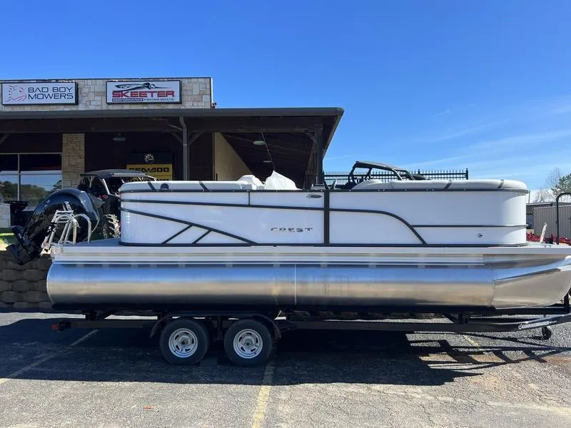 The Image of 2023 Crest Classic LX 220 SLC pontoon boat on a trailer in a parking lot. - 0