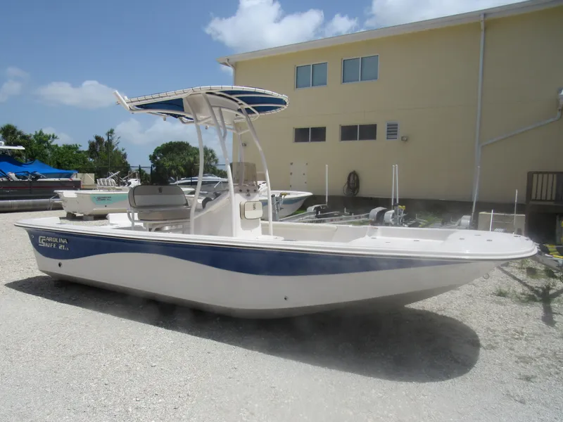 Slide: The Image of 2022 Carolina Skiff 21 LS boat with T-top, parked on gravel near a building. - 24