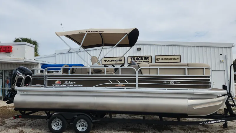 The Image of 2023 Sun Tracker SportFish 22 DLX pontoon boat on a trailer outside dealership. - 0