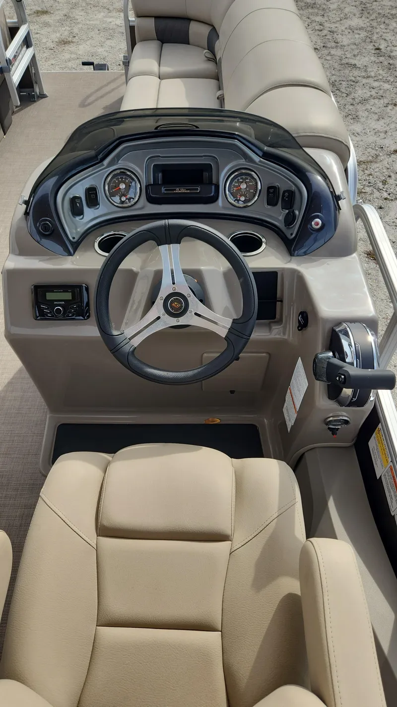 Slide: The Image of 2023 Sun Tracker SportFish 22 DLX boat cockpit with steering wheel and beige seating. - 2