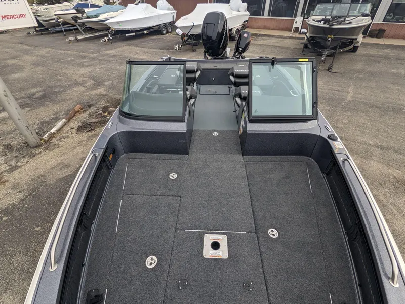 Slide: The Image of 2025 Lund 219 Pro V Fiberglass boat, open deck view, parked in a marina. - 6