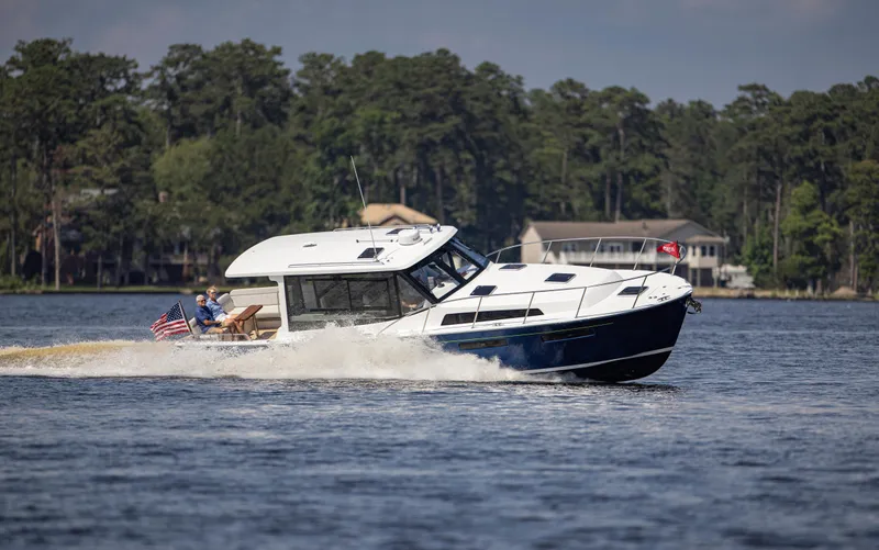 Slide: The Image of 2025 MJM 42 boat cruising on a lake with trees and houses in the background. - 2