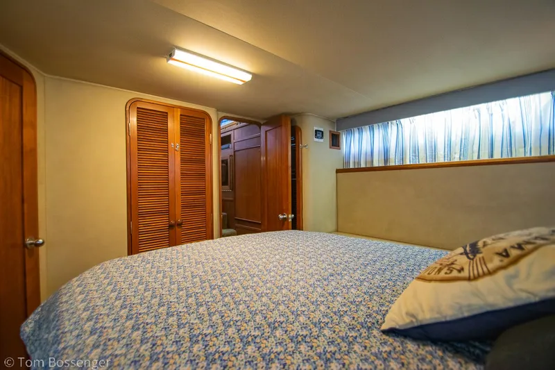 Slide: The Image of 1986 Chris-Craft Corinthian cabin interior with bed, wooden cabinets, and window curtains. - 23